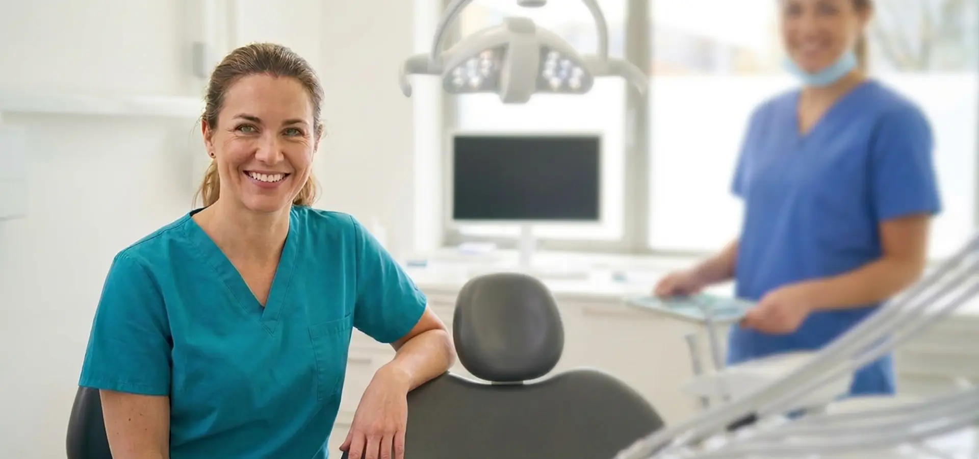 A happy dentist and dental technician in the detal surgery next to the dentists chair and lights illustrating the high quality shredding service dentists receive from PaperMountains