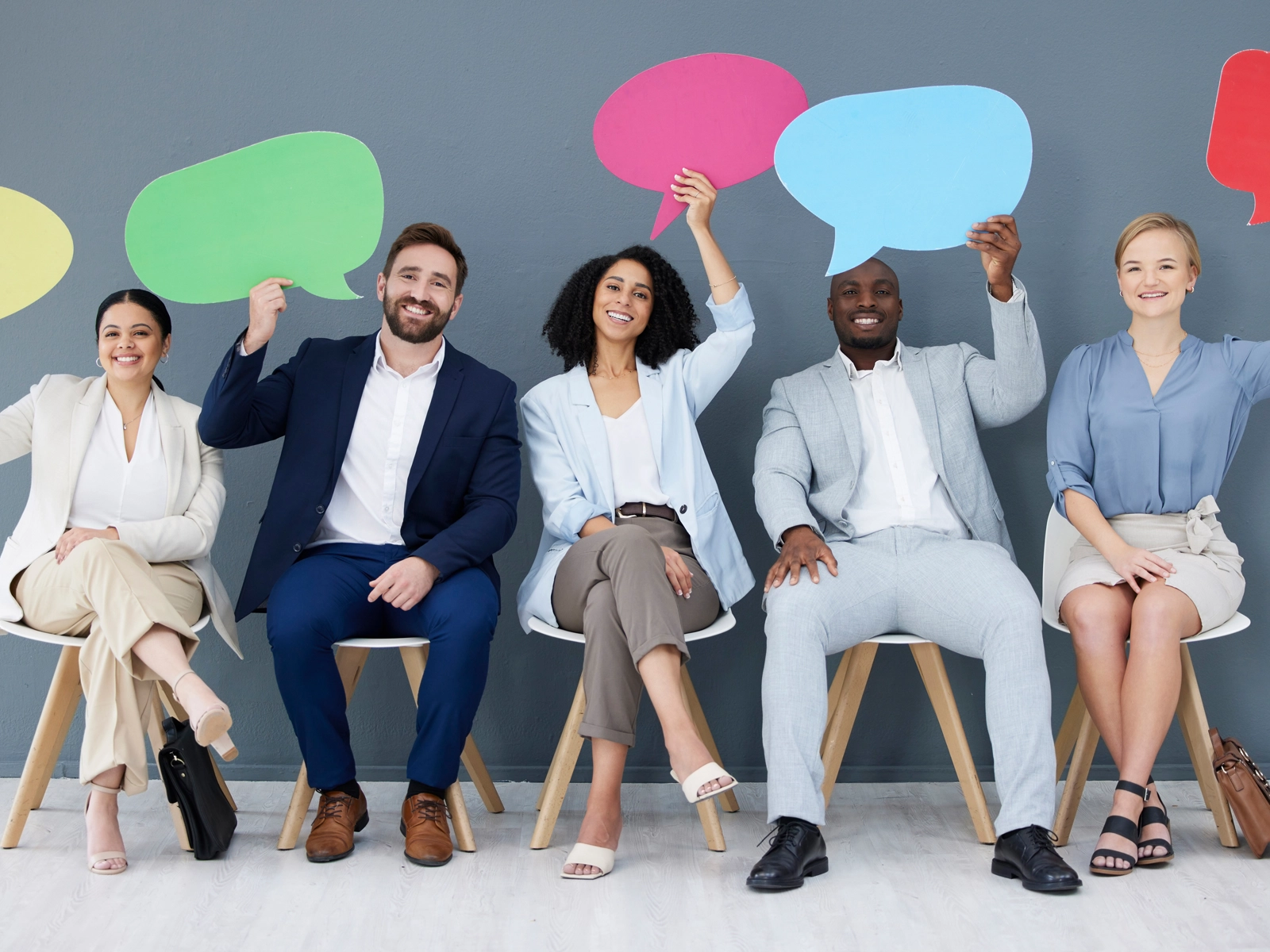employees sittting in a row holding coloured cardboard speach bubbles above their heads illustrating them having their say in a employee survey