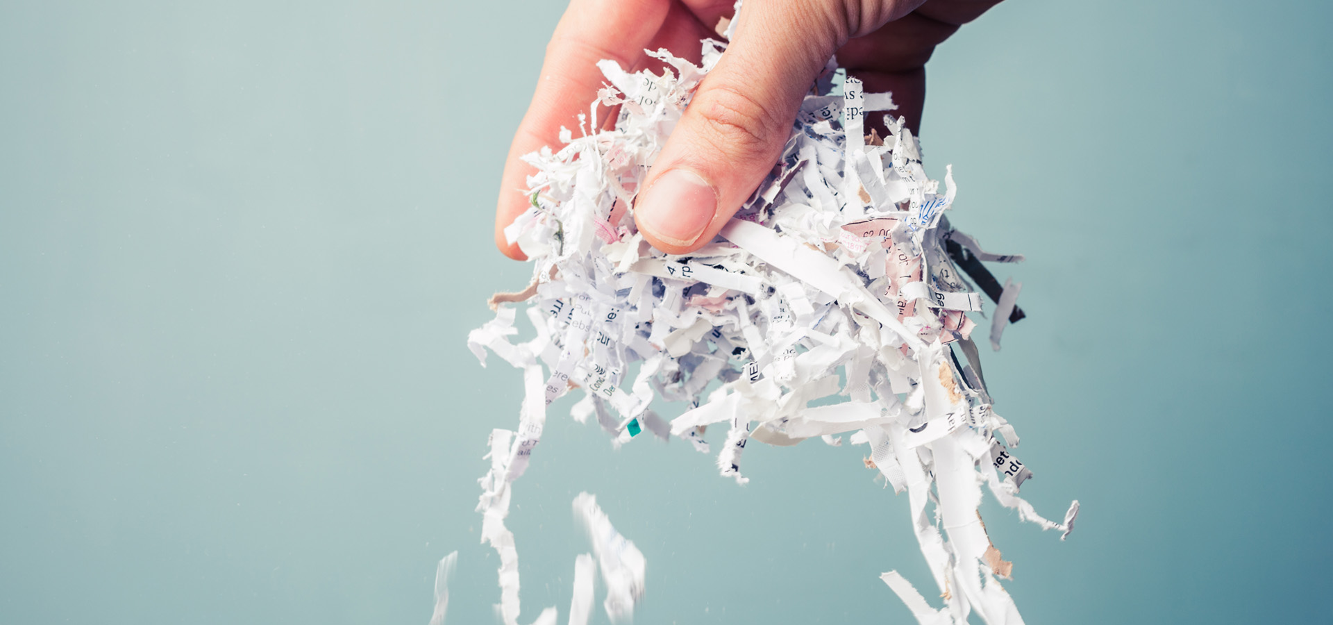 A Hand pinching asecurity shredded paper and held over a blue background.