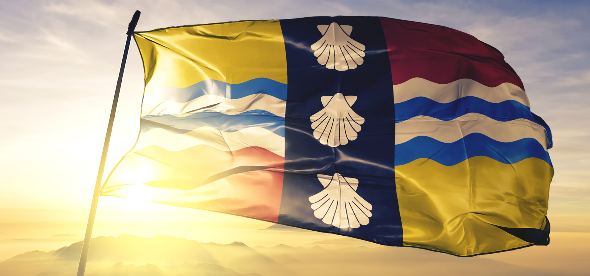 The Flag Of Bedfordshire Flying On A Flag Pole In Front Of A Bright Sunrise